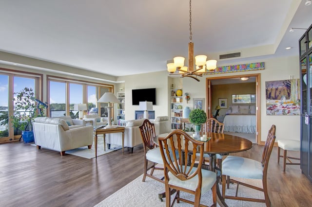 Living and dining area with large windows overlooking water and a glimpse of the bedroom.
