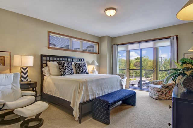 King bed with white linens, zebra print pillows, and a blue bench in a bedroom with a large sliding glass door and a window.