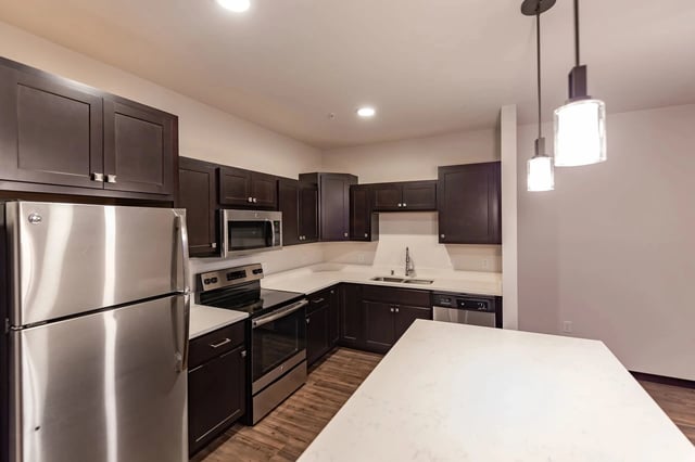 Modern kitchen with dark wood cabinets, stainless steel appliances, and white countertops.