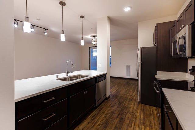 Kitchen island with sink and faucet, dark cabinets, and stainless steel appliances.