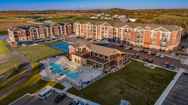 Aerial view of apartment complex buildings, pool, tennis court, and parking lot.