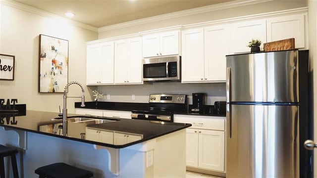 Modern kitchen with stainless steel appliances, white cabinets, and a dark granite island countertop.