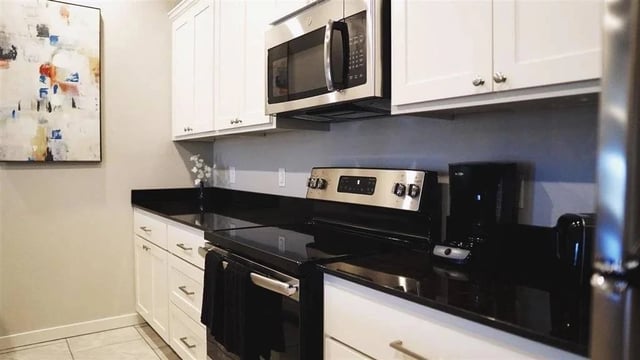 Modern kitchen with stainless steel appliances, white cabinetry, and black granite countertops.
