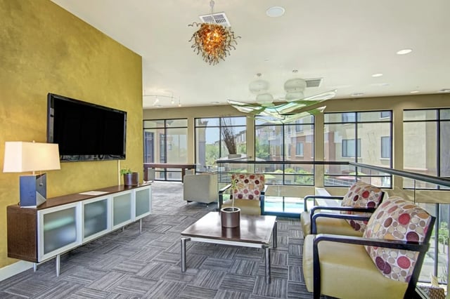 Modern lounge area with a TV, comfortable seating, and large windows overlooking a pool.