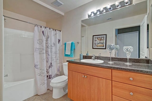 Modern bathroom vanity with wood cabinets, granite countertops, and a large mirror.
