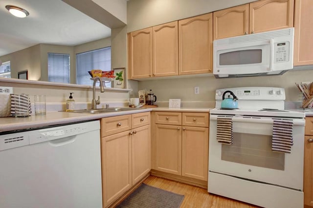 Kitchen with light wood cabinets, white appliances including a dishwasher, stove, and microwave.