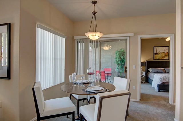 Dining area with a round table set for dinner, leading to a bedroom with a king-sized bed.