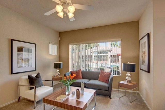 Living room with gray sofa, white armchair, coffee table, and window view of community.