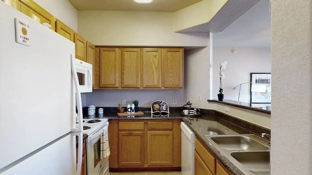 Kitchen with white refrigerator, oven, microwave, wooden cabinets, and granite countertops.