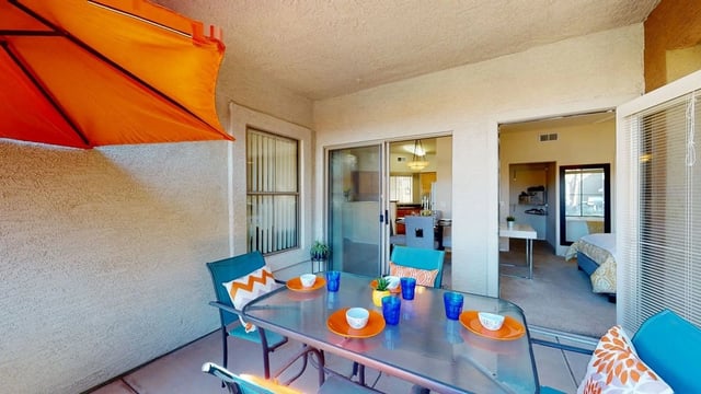 Patio dining set with orange umbrella, view into living room and bedroom.
