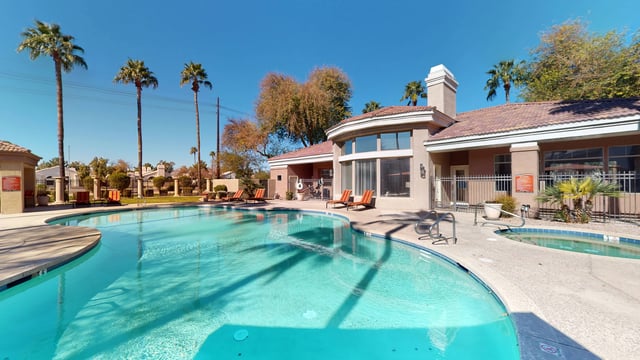 Resort-style swimming pool and spa with lounge chairs and palm trees.