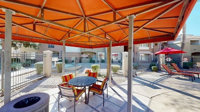 Outdoor seating area with a table and chairs under an orange canopy, next to lounge chairs and a red umbrella.