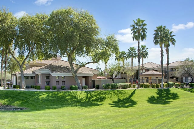 Apartment building exterior with palm trees and manicured lawn.