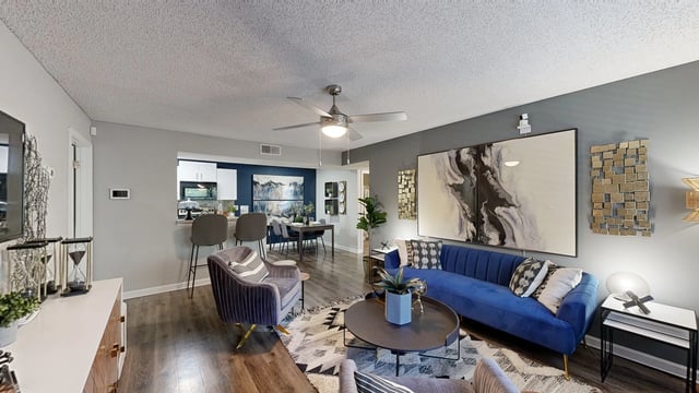 Modern living room and dining area with blue couch, accent chairs, and contemporary art.