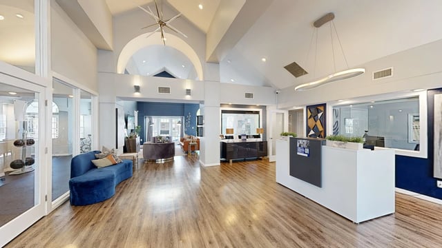 Spacious, modern apartment building lobby with a reception desk, seating area, and gym access.