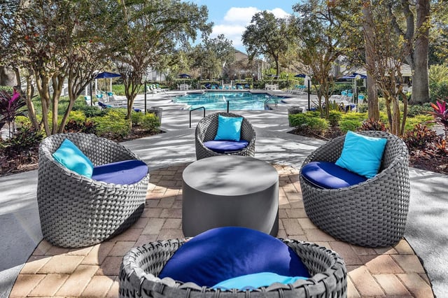 Outdoor seating area with wicker chairs and a table in front of a swimming pool.