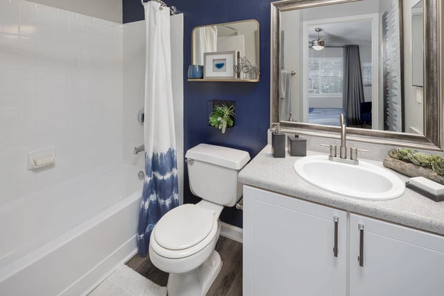 Modern bathroom with navy blue accent wall, white tiled shower and tub, and sleek vanity with sink.