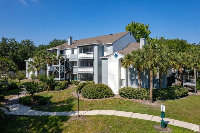 Exterior view of apartment buildings with palm trees and green landscaping.