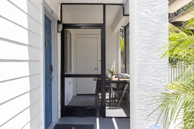 Exterior view of an apartment building entrance with a blue door, screen door, and small patio area.