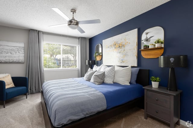 A bedroom with a king-size bed, navy blue accent wall, and large window.