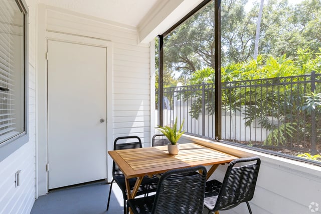 Screened-in balcony with a table and four chairs, overlooking lush greenery.