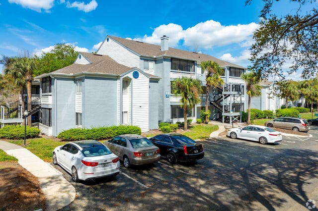 Exterior view of an apartment building with a parking lot in front.