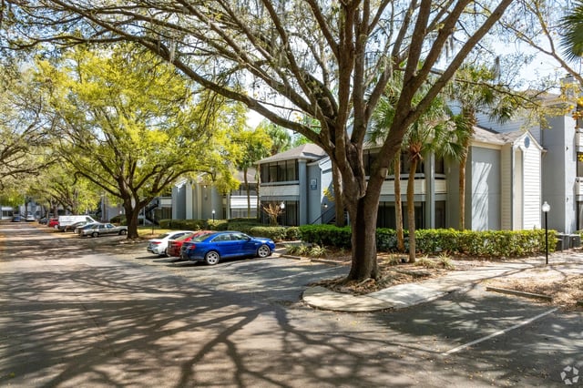 Apartment complex exterior with parking lot and trees.
