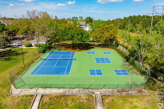 Tennis and pickleball courts with blue playing surfaces and green out-of-bounds areas, surrounded by a fence.