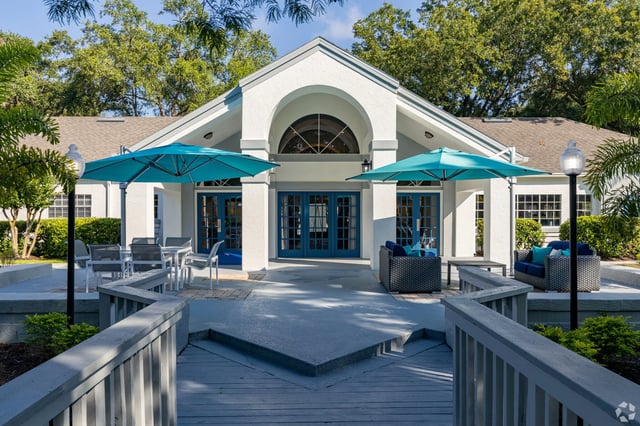 Building entrance with blue doors and teal umbrellas, outdoor seating area.