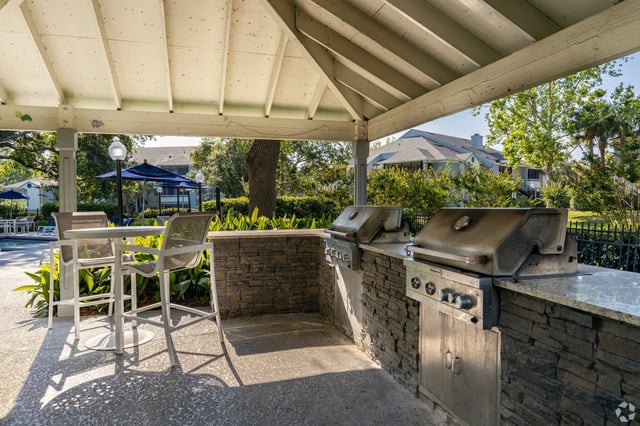 Outdoor grilling area with two stainless steel grills and a stone counter, next to a table and chairs.