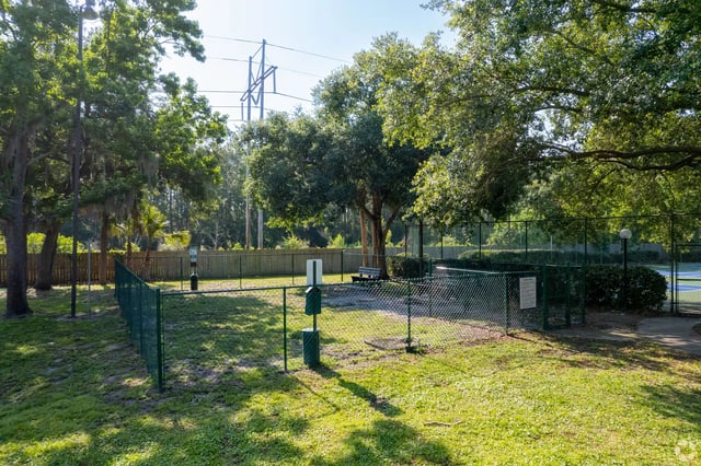 Enclosed dog park area with green fencing, grass, and trees.