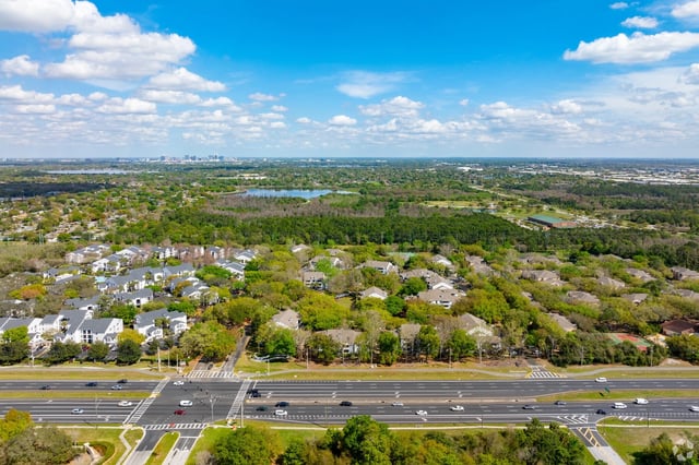 Aerial view of a sprawling suburban neighborhood with dense trees and a highway in the foreground.