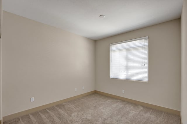 Empty bedroom with beige walls, neutral carpet, and a large window with blinds.
