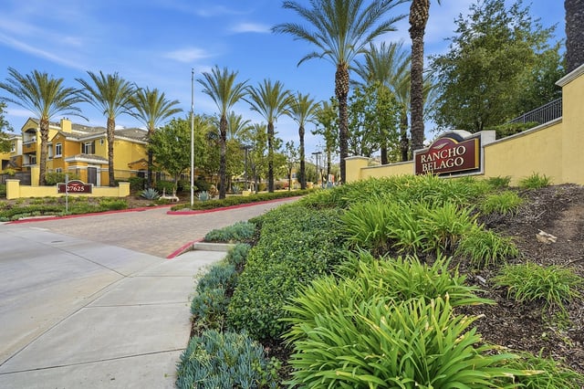 Rancho Belago property entrance with palm trees and lush landscaping.