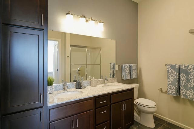 Double vanity bathroom with granite countertops, dark wood cabinets, and tiled flooring.