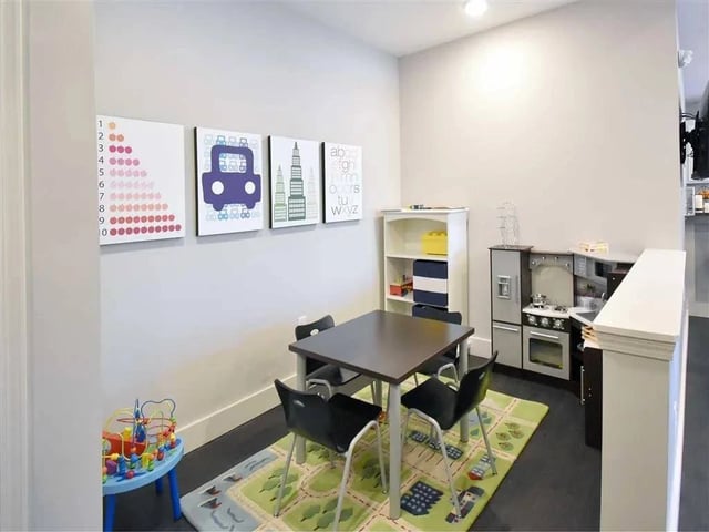 Children's playroom with a table, chairs, toy kitchen, and educational wall art.