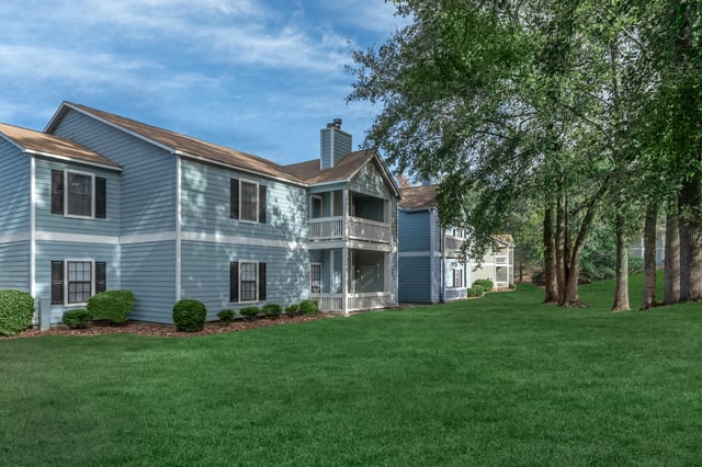 Exterior view of apartment buildings with blue siding and green lawns.