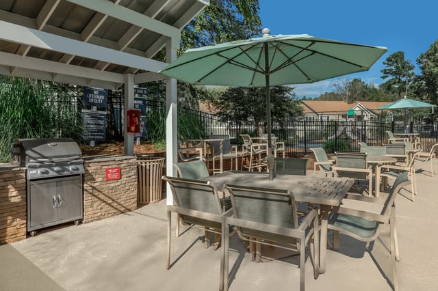 Outdoor grilling station with tables and umbrellas by the pool.