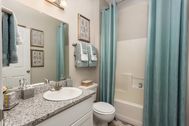 Modern bathroom with granite countertop, white sink, toilet, and bathtub with teal shower curtain.