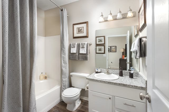 Modern bathroom with a white bathtub, toilet, and vanity with a granite countertop.