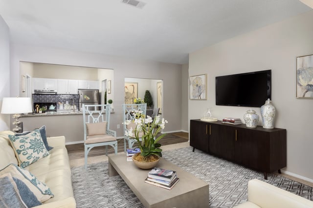 Modern living room with a couch, coffee table, and TV, opening to a kitchen.