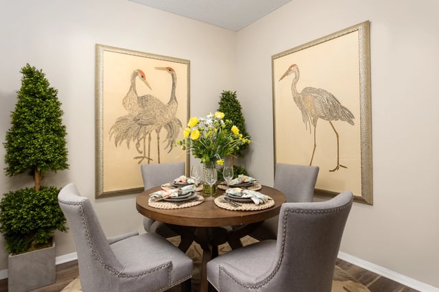 Dining area with round table, chairs, and art featuring cranes.