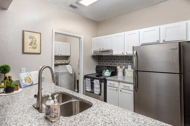 Kitchen with granite countertops, stainless steel appliances including a refrigerator and stove, white cabinets, and a separate laundry area with a washer and dryer.