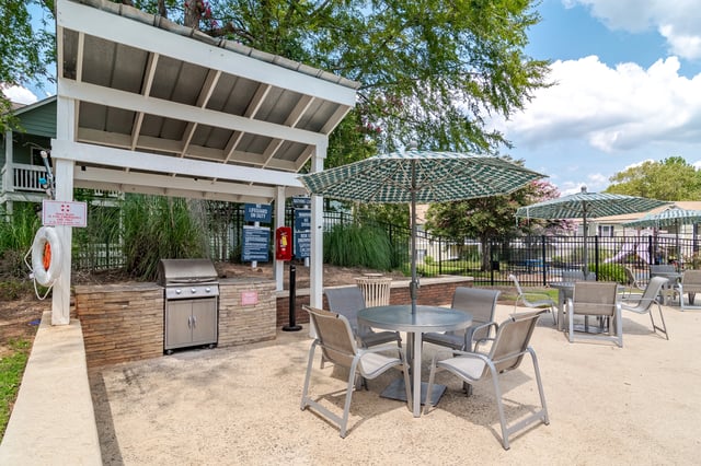 Outdoor grilling station with a stainless steel grill, stone counter, and seating area with umbrellas.