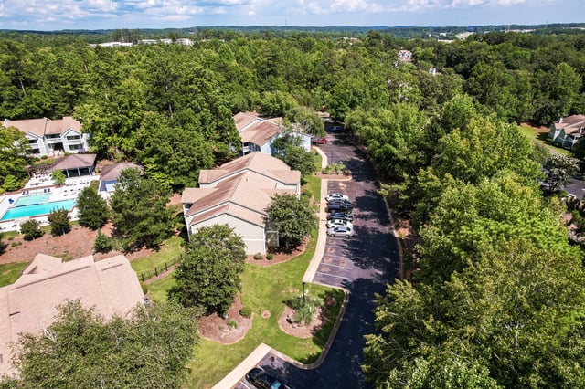 Aerial view of apartment buildings with a swimming pool and parking lot surrounded by trees.