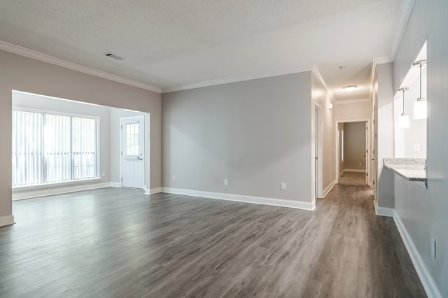Spacious living room with wood-look flooring, neutral walls, and large windows.
