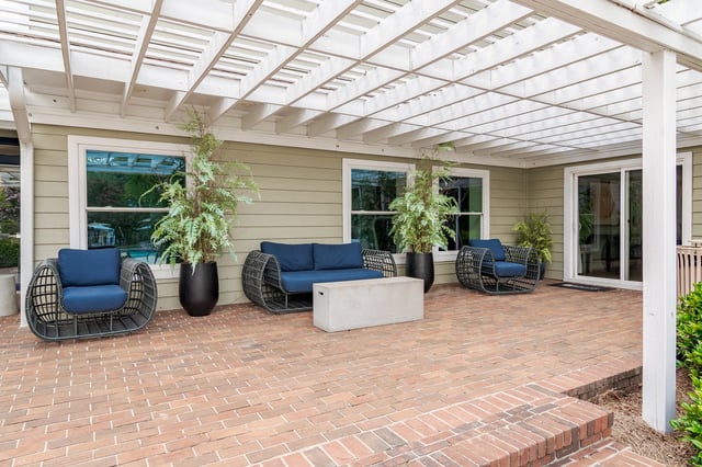 Outdoor patio area with wicker furniture and plants under a white pergola.