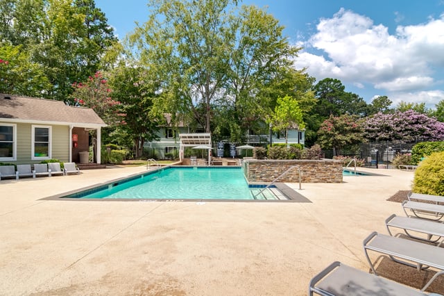 Outdoor swimming pool with lounge chairs and surrounding trees and buildings.