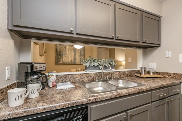 Modern kitchen with gray cabinets, stainless steel sink, and coffee maker.