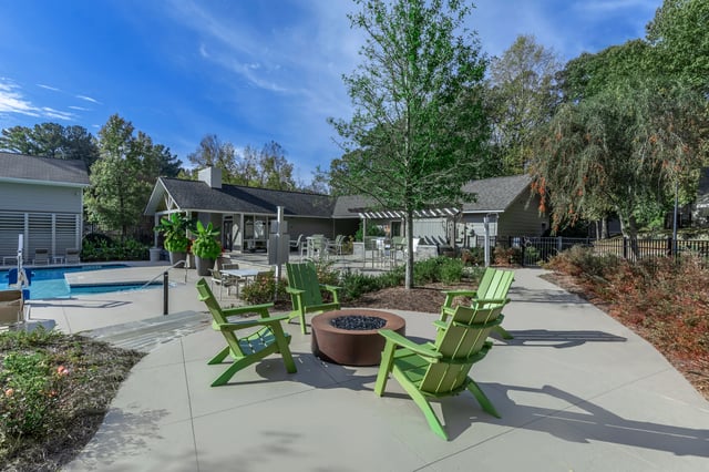 Patio with green chairs around a fire pit, next to a swimming pool and building.